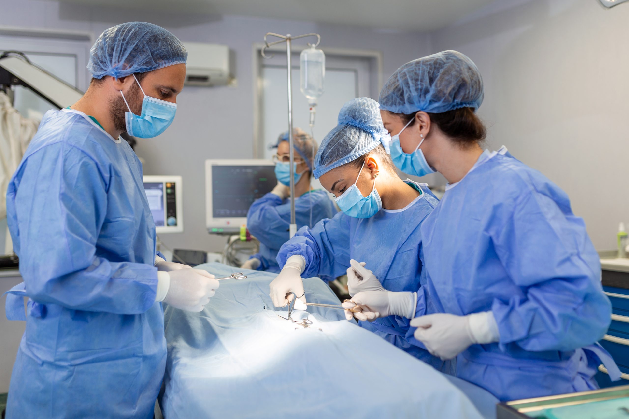 Surgeons operating below lighting equipment. Male and female doctors are wearing blue scrubs. They are working in hospital.